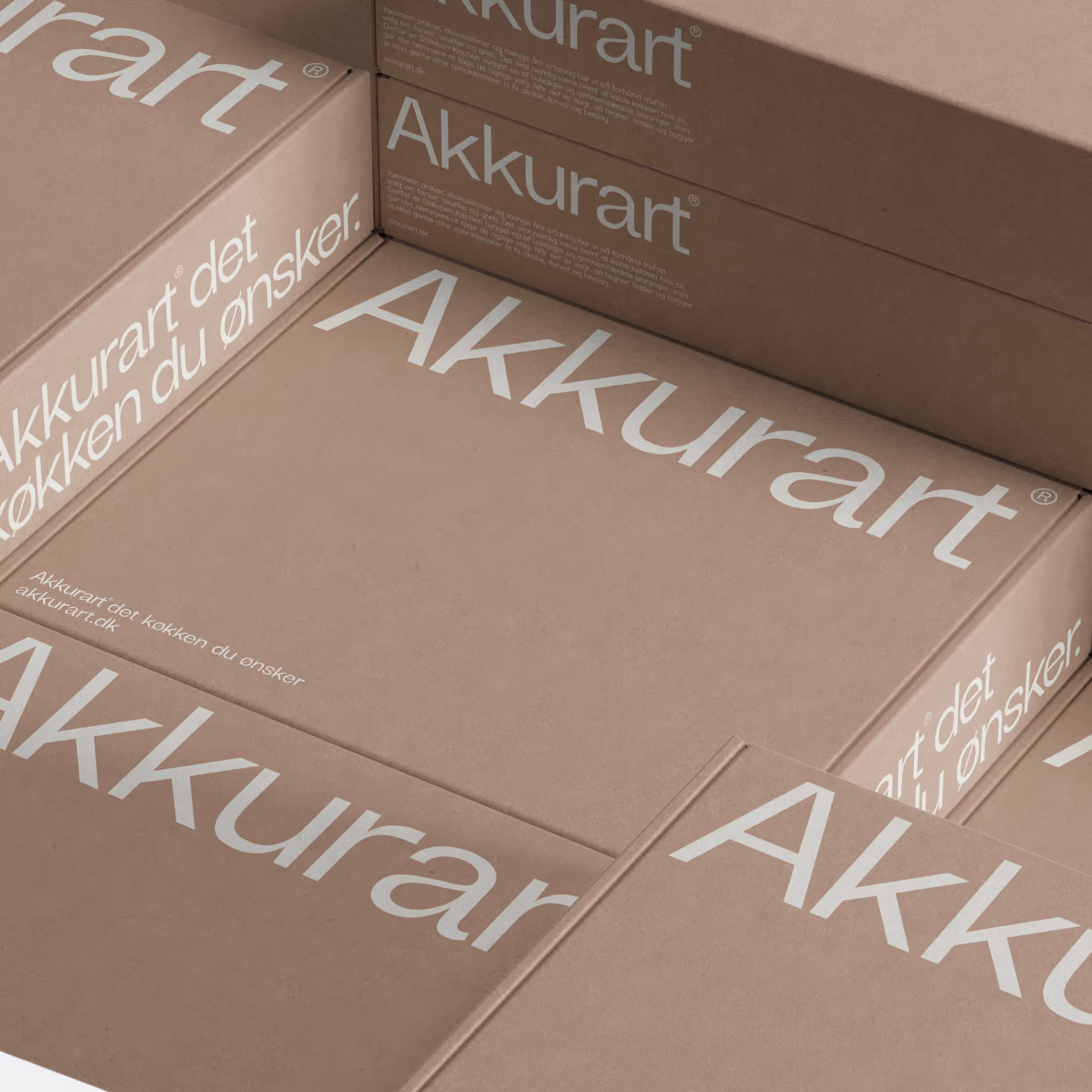 Stablet brun papkasse med teksten 'Akkurart' og 'Akkurart det køkken du ønsker' trykt i hvidt.