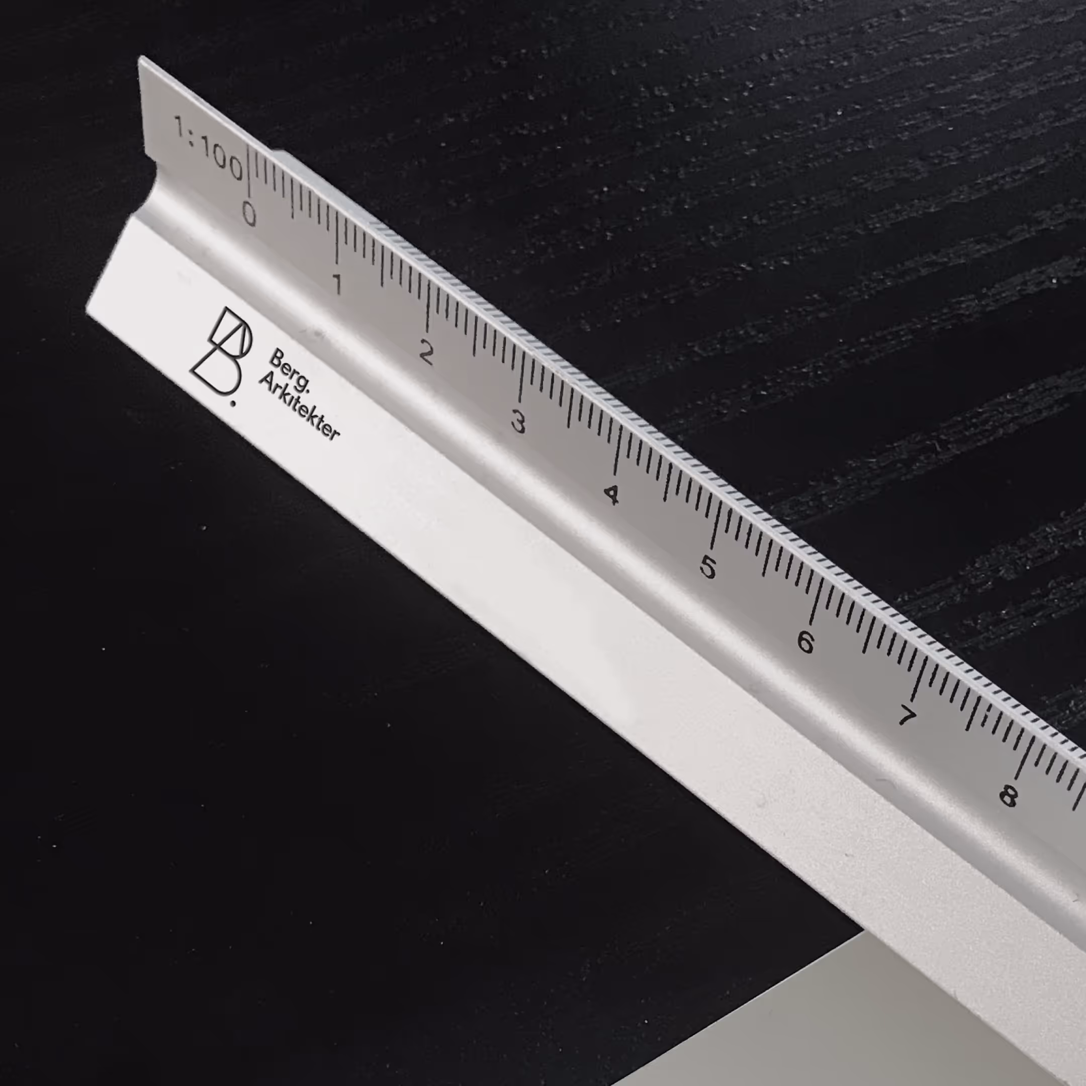 Aluminiumsblok med indgravering af lineal og teksten Berg Arkitekter på sort bord.
