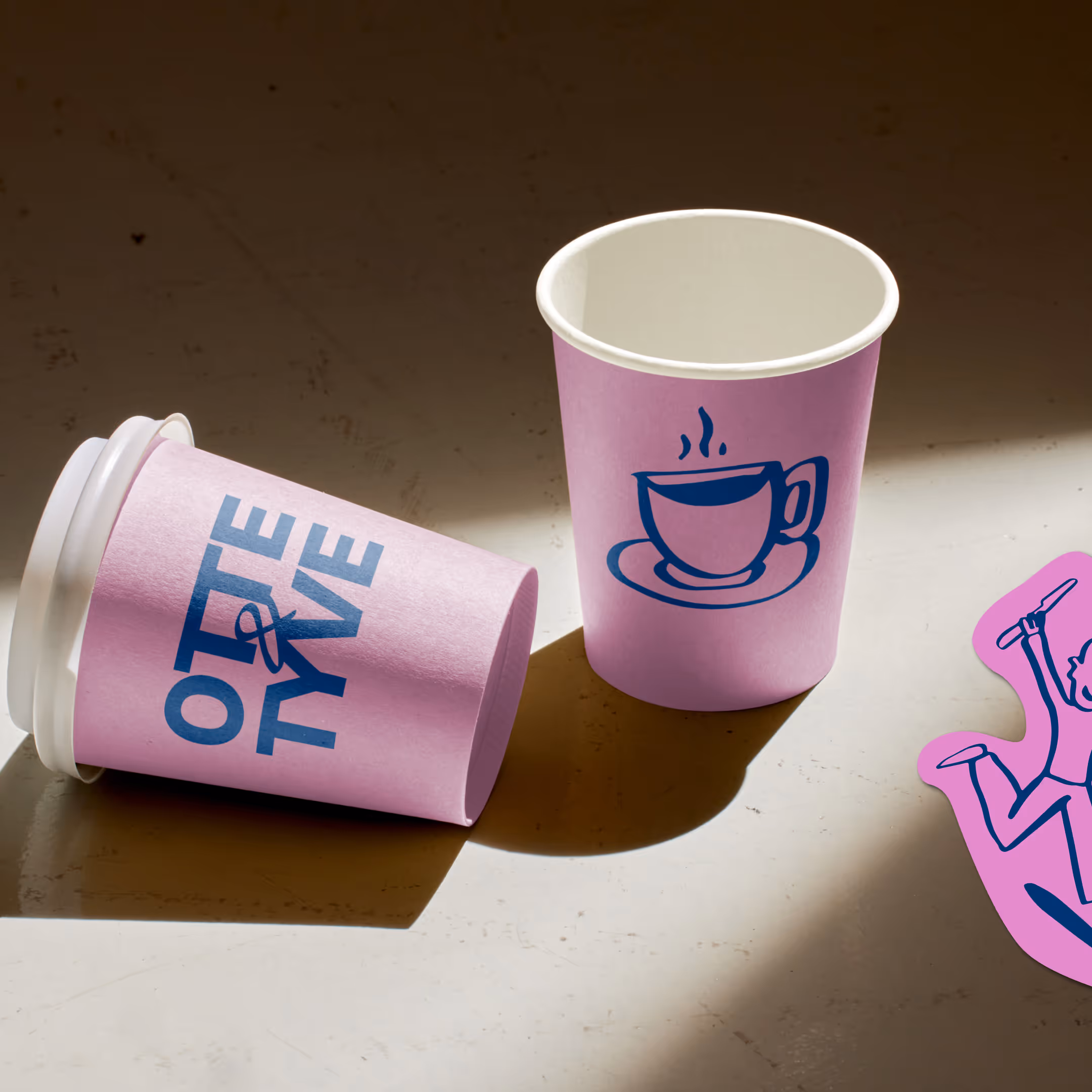To lyserøde kaffekrus, ét med tekst Otte & Tyve, det andet med blå kop og underkop illustration.