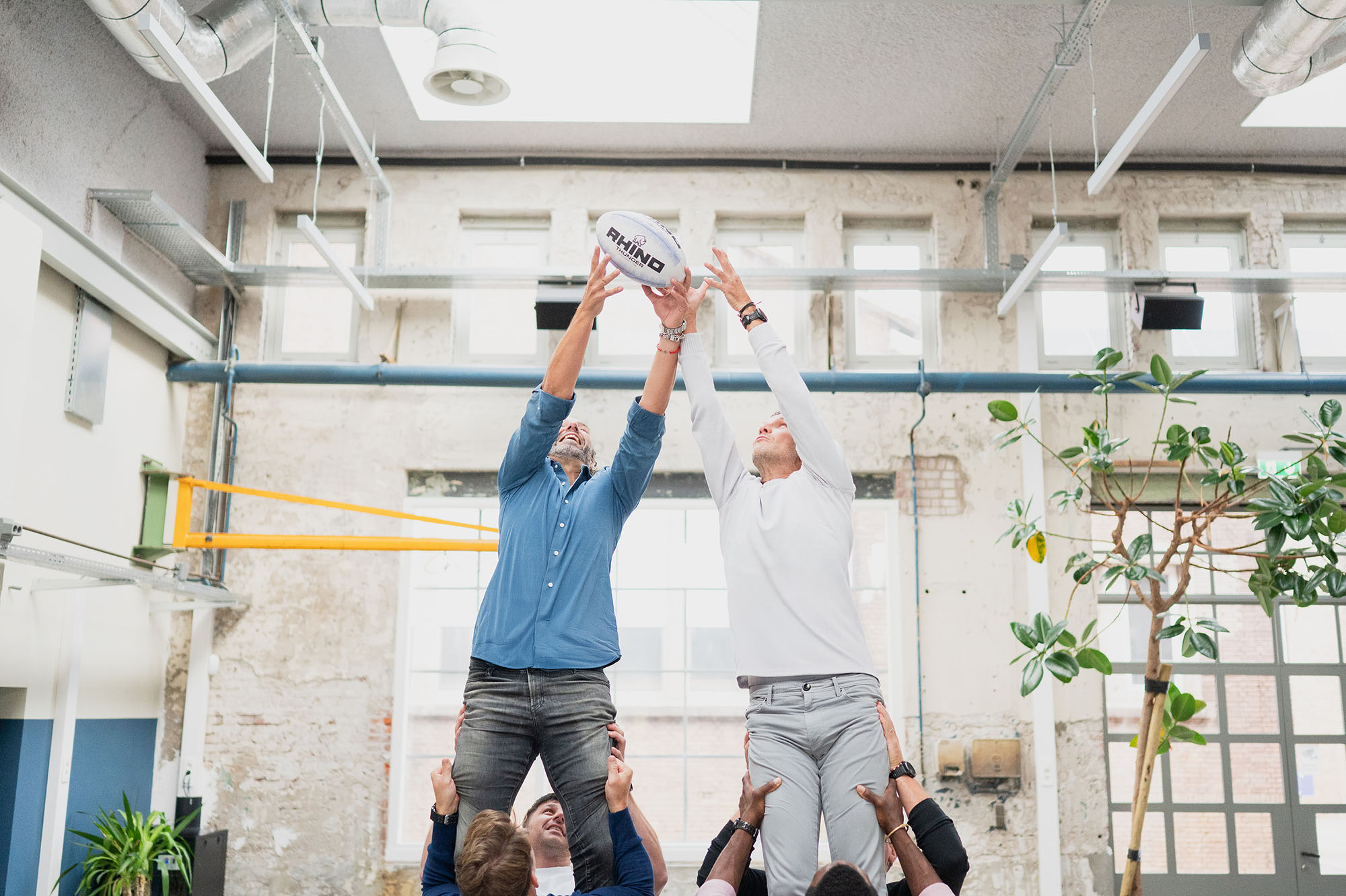 Twee deelnemers van de Qube worden door teamgenoten opgetild. Een 'lineout', een rugby trem waarbij spelers worden opgetild om de bal te vangen. Een metafoor voor teamontwikkeling binnen de Qube.