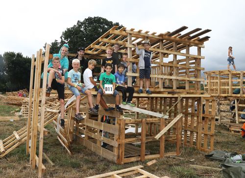 Groep kinderen met leider bouwen aan een hut van pallets