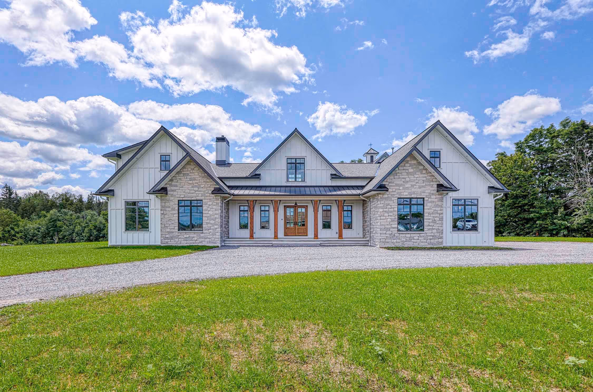 Exterior of white, modern home featuring vertical siding, stone work, and wooden pillars.