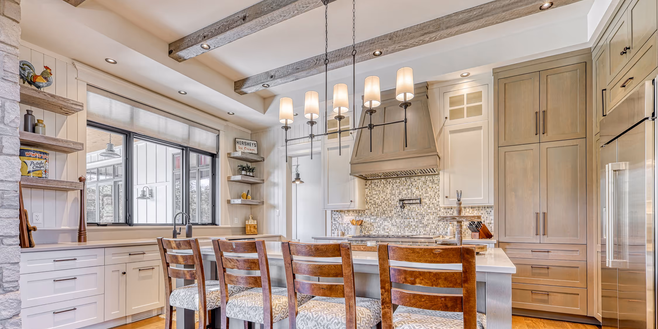 Large kitchen with wood, greyish wood beams on the ceiling, and a large kitchen island with 4 bar stools.