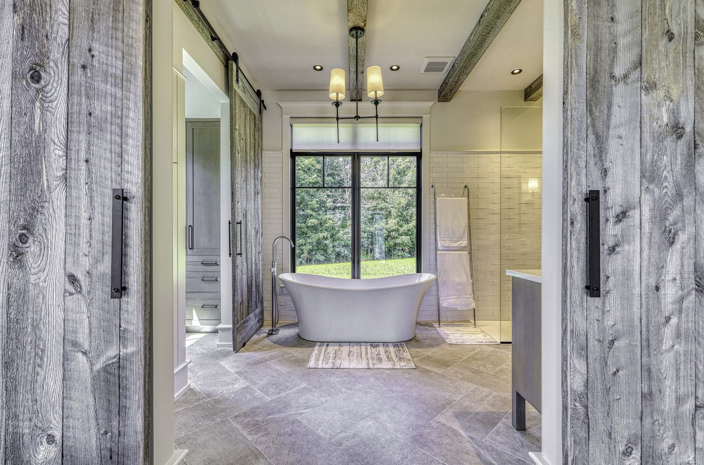 A large open bathroom with a standalone tub, two vanities, and a large window.