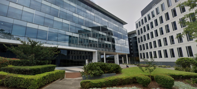F1 building is glass, next to a white building and has greenery outside