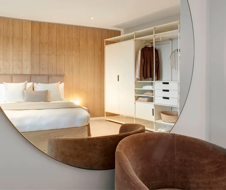 A modern bedroom with wood paneling, open wardrobe, and a round mirror reflecting the space.