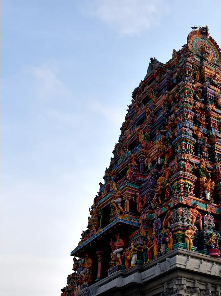 A vibrant, intricately carved Hindu temple gopuram rises against a clear blue sky.
