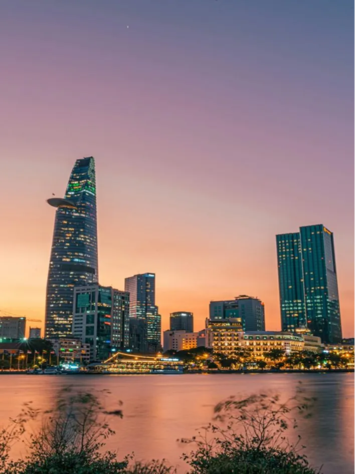 A vibrant cityscape at sunset featuring modern skyscrapers and a calm waterfront.