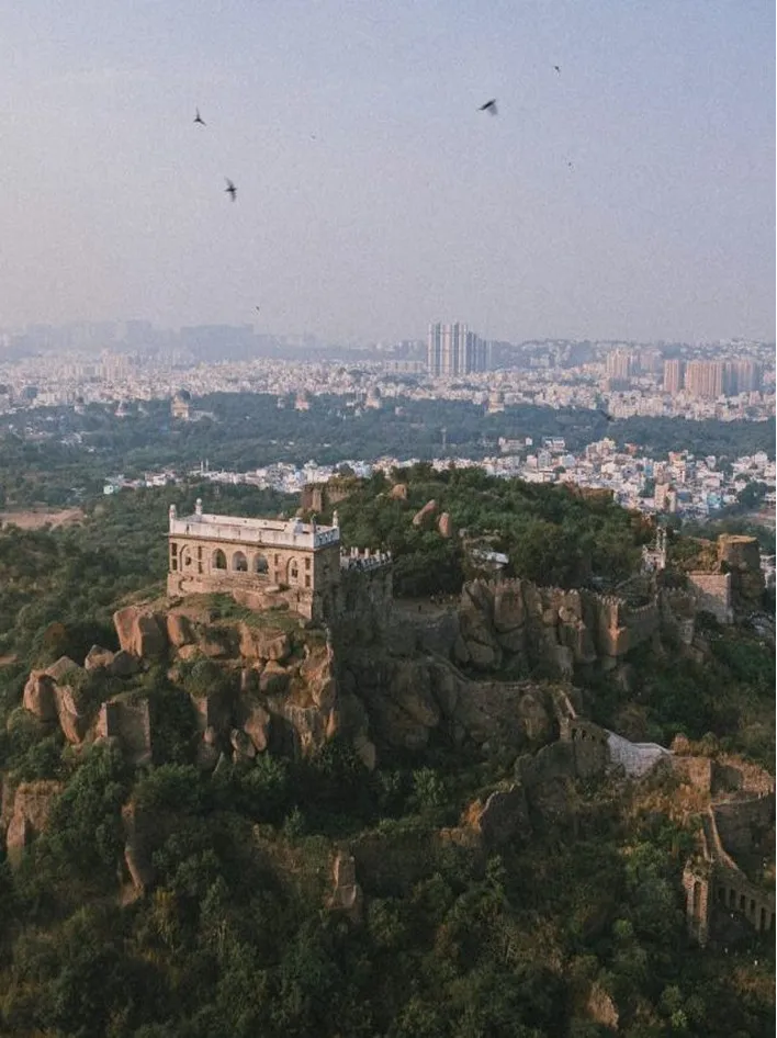 A historic fort atop rocky terrain overlooks a sprawling urban cityscape under a clear sky.
