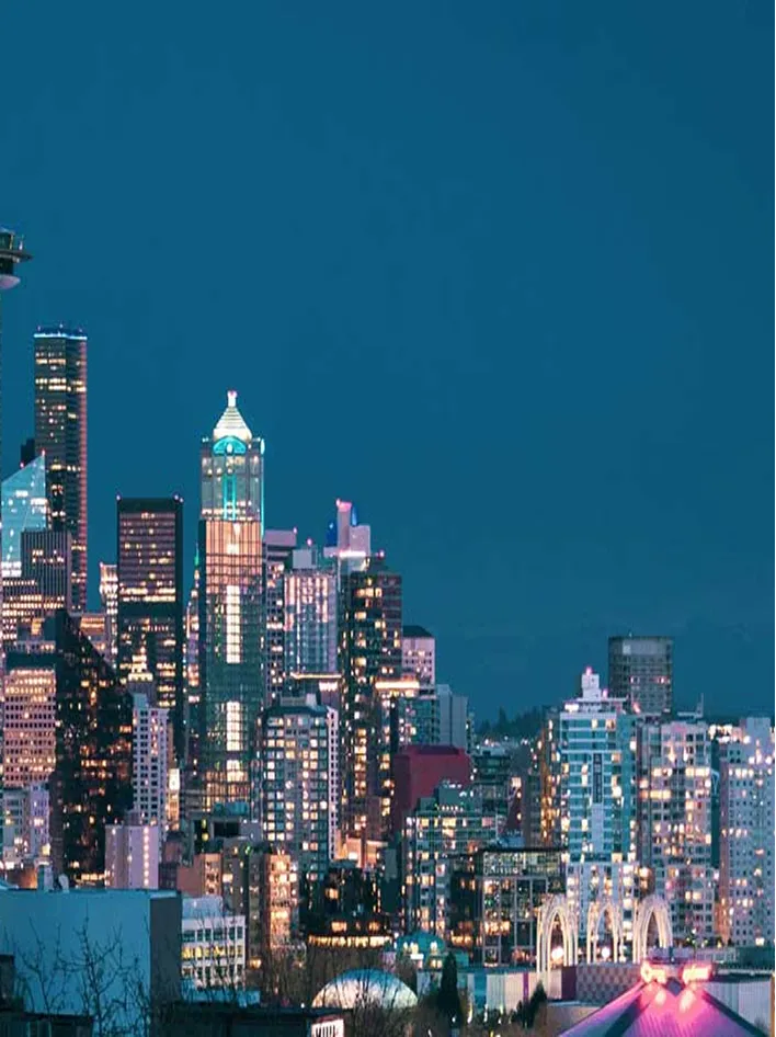 A vibrant city skyline at night, illuminated by glowing lights against a deep blue sky.
