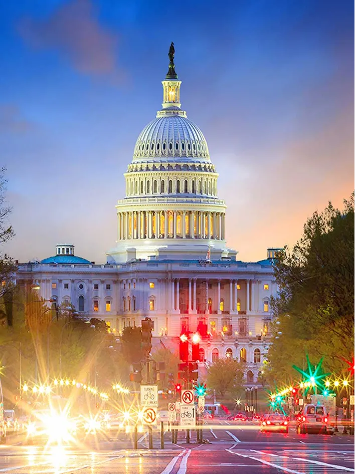 The U.S. Capitol illuminated at dusk, with vibrant city lights and traffic in the foreground.