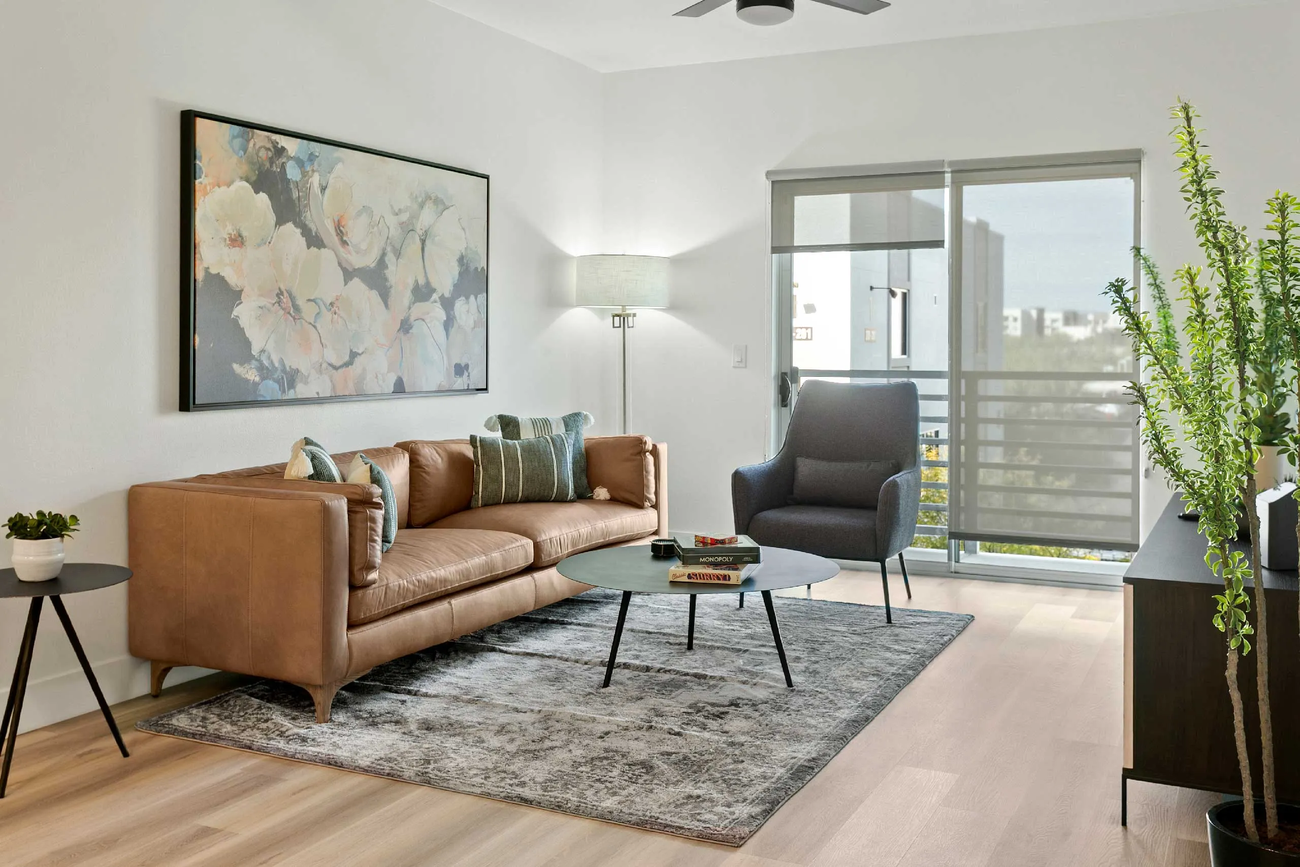 Modern living room with a leather sofa, armchair, abstract art, and natural light.