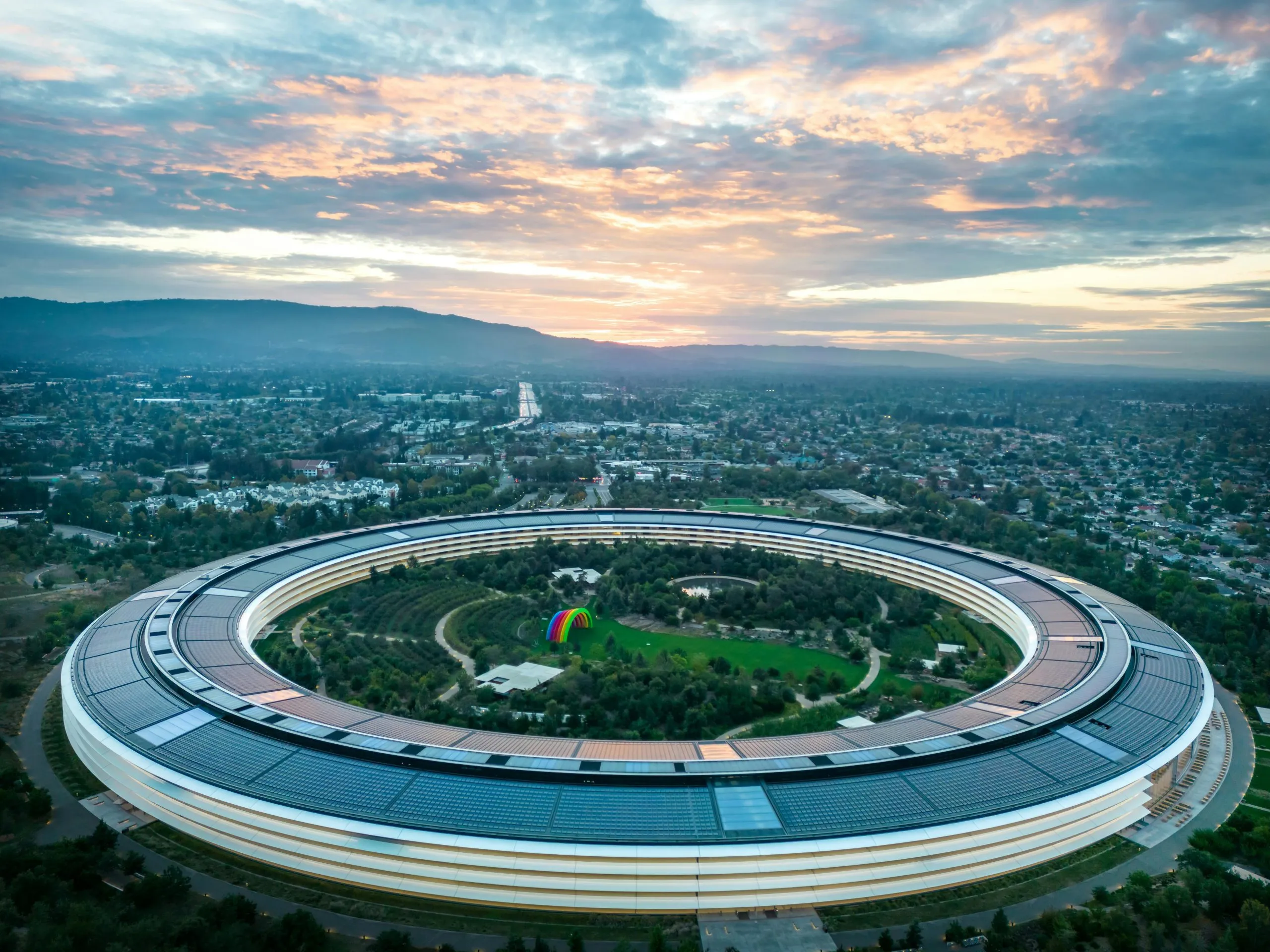 Apple Park's circular building in Cupertino, California, surrounded by greenery at sunset.