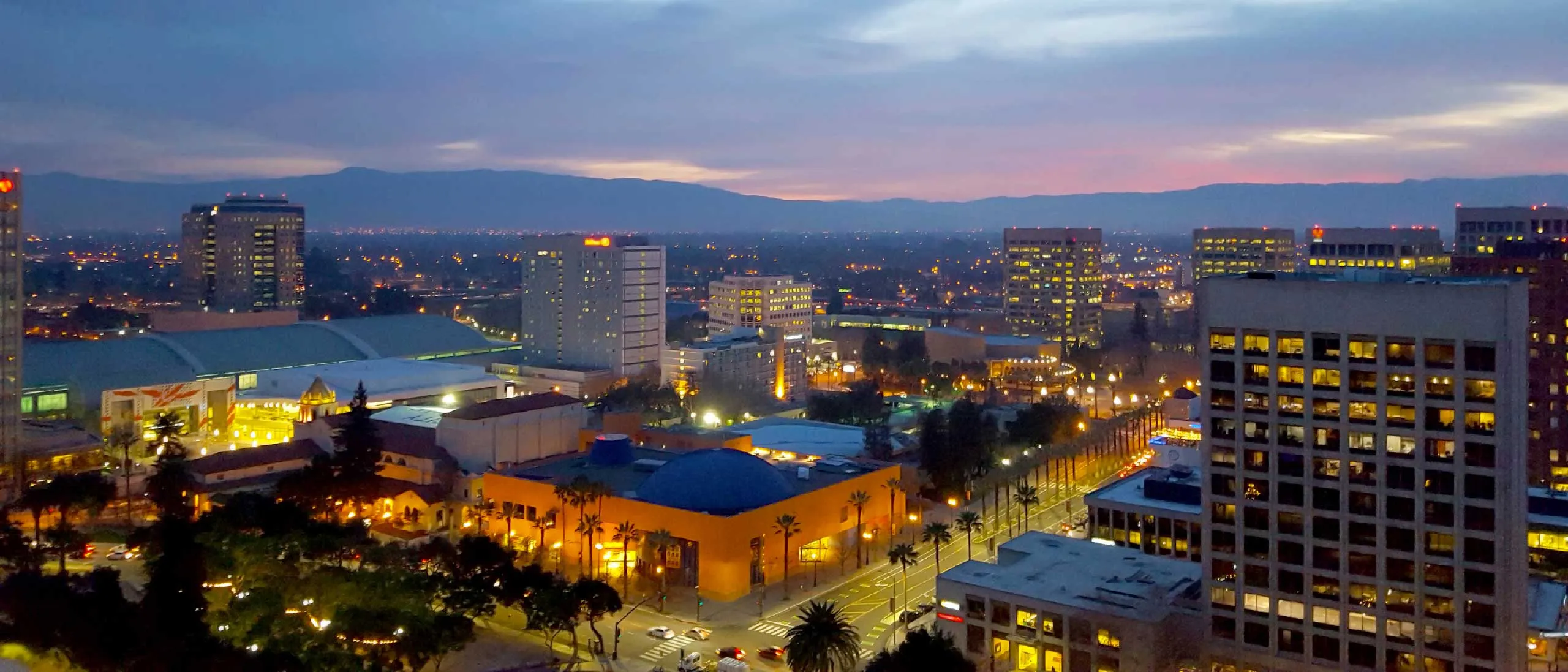 A vibrant cityscape at dusk, featuring illuminated buildings and streets in San Jose, California.