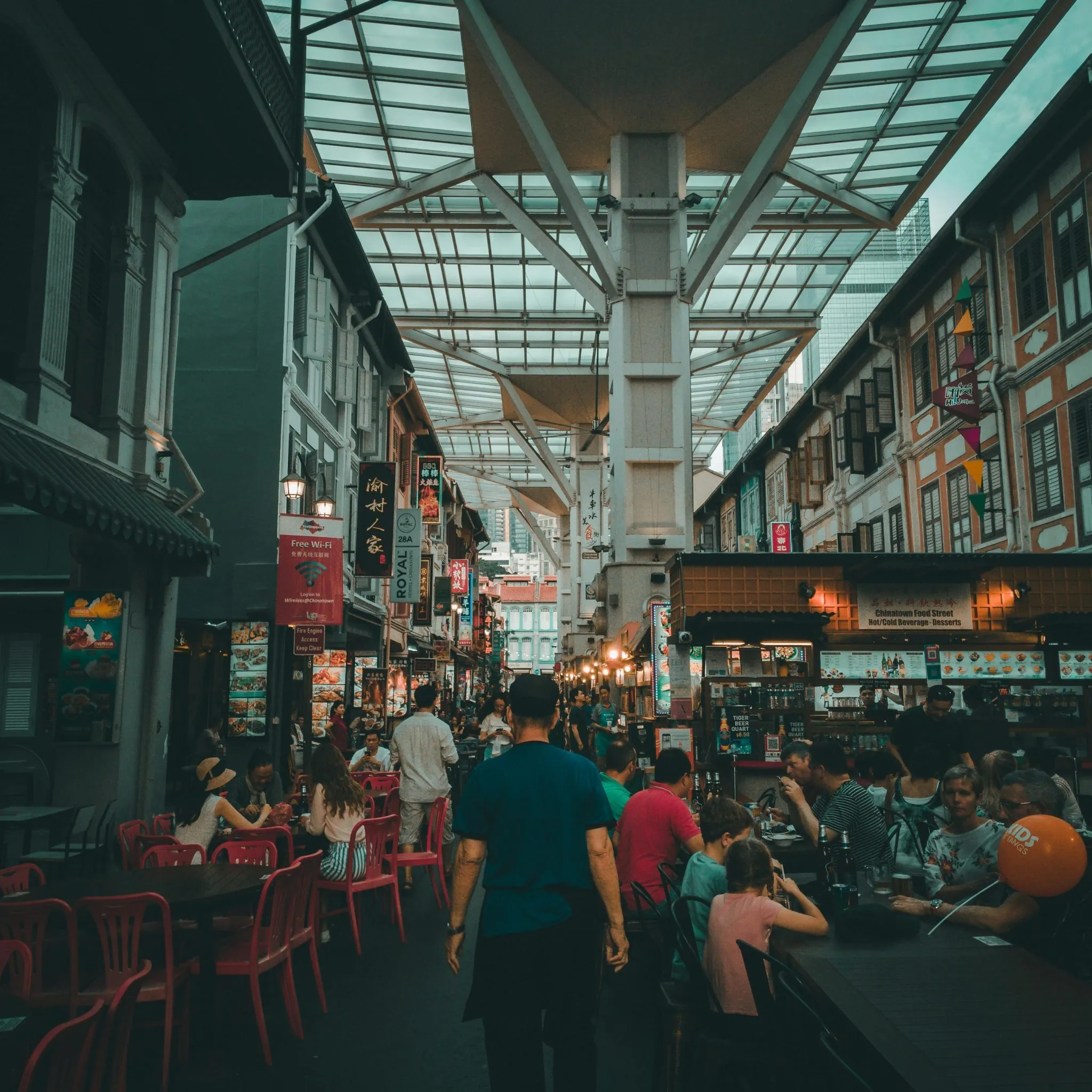 A bustling covered street market with vibrant dining areas and traditional-style buildings.