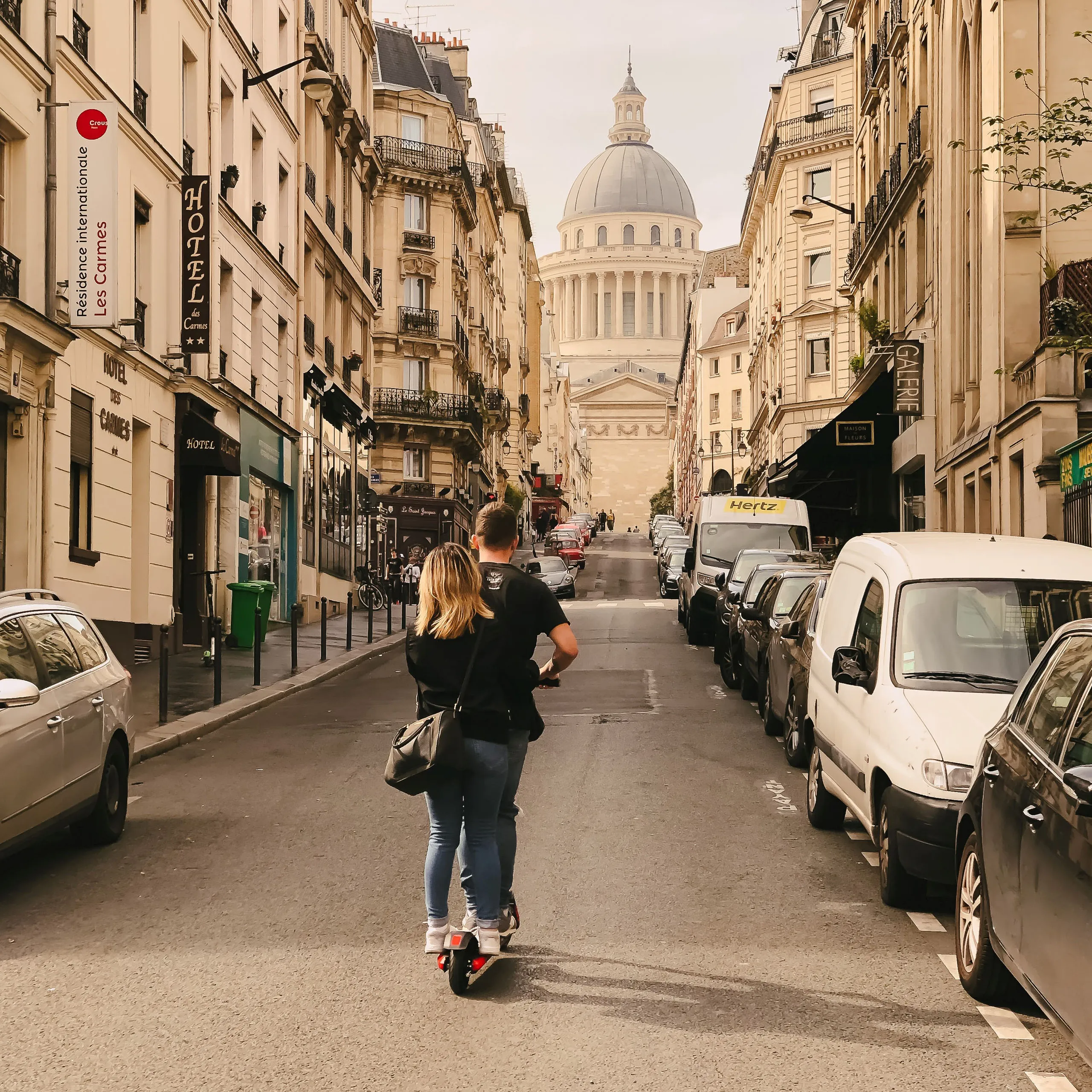 A couple rides a scooter down a Parisian street, with the Panthéon visible in the background.
