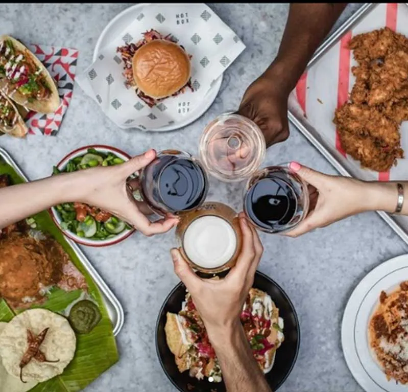 A table with diverse dishes and drinks, with hands raising glasses in a celebratory toast.