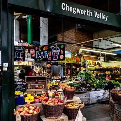 Chegworth Valley market stall displays fresh produce, juices, and vibrant fruits in a rustic setting.