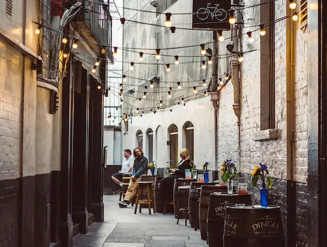 A narrow alleyway with string lights, outdoor seating, and people enjoying a casual atmosphere.