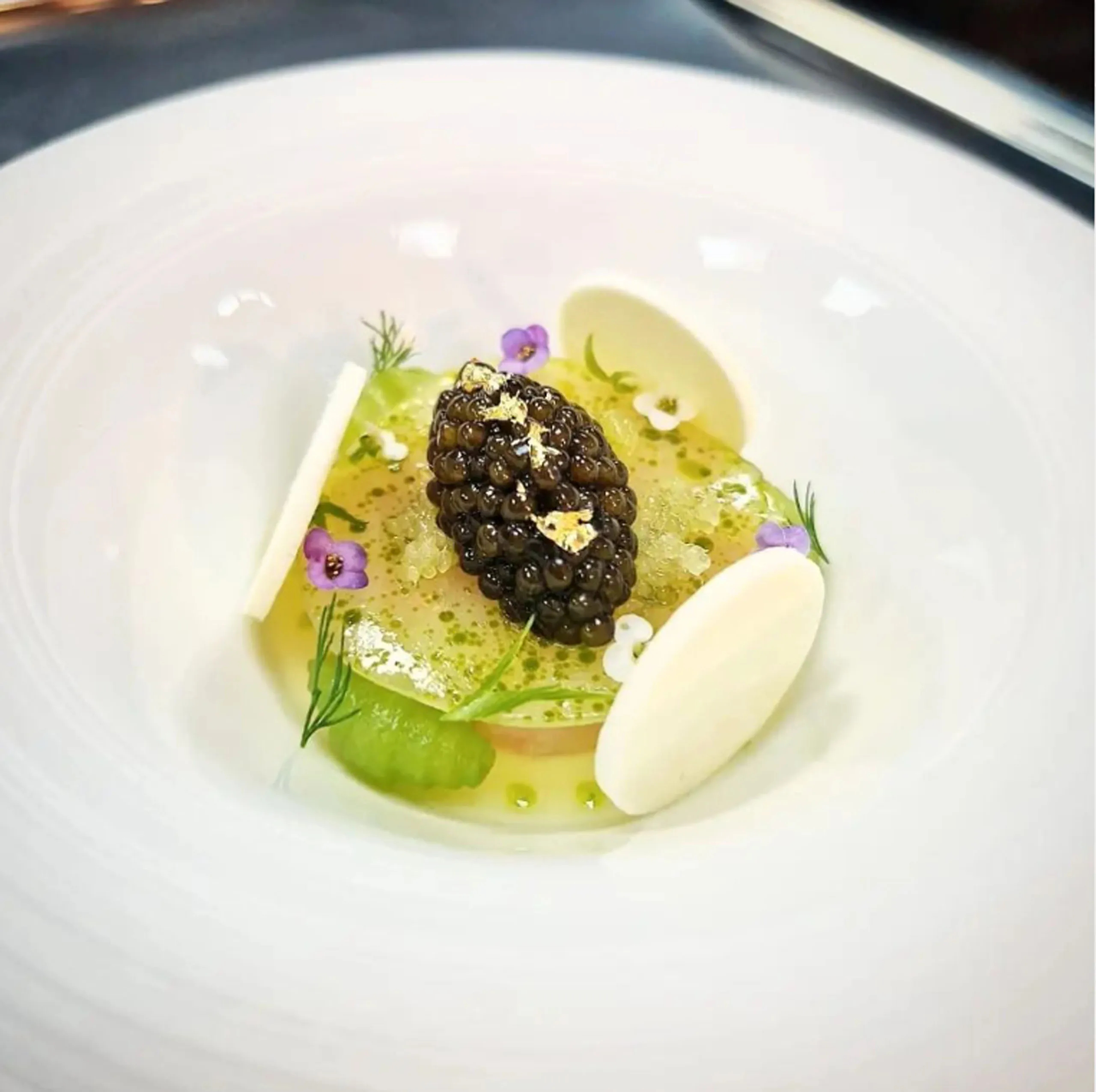 A refined dish featuring caviar, edible gold, delicate garnishes, and artistic plating.