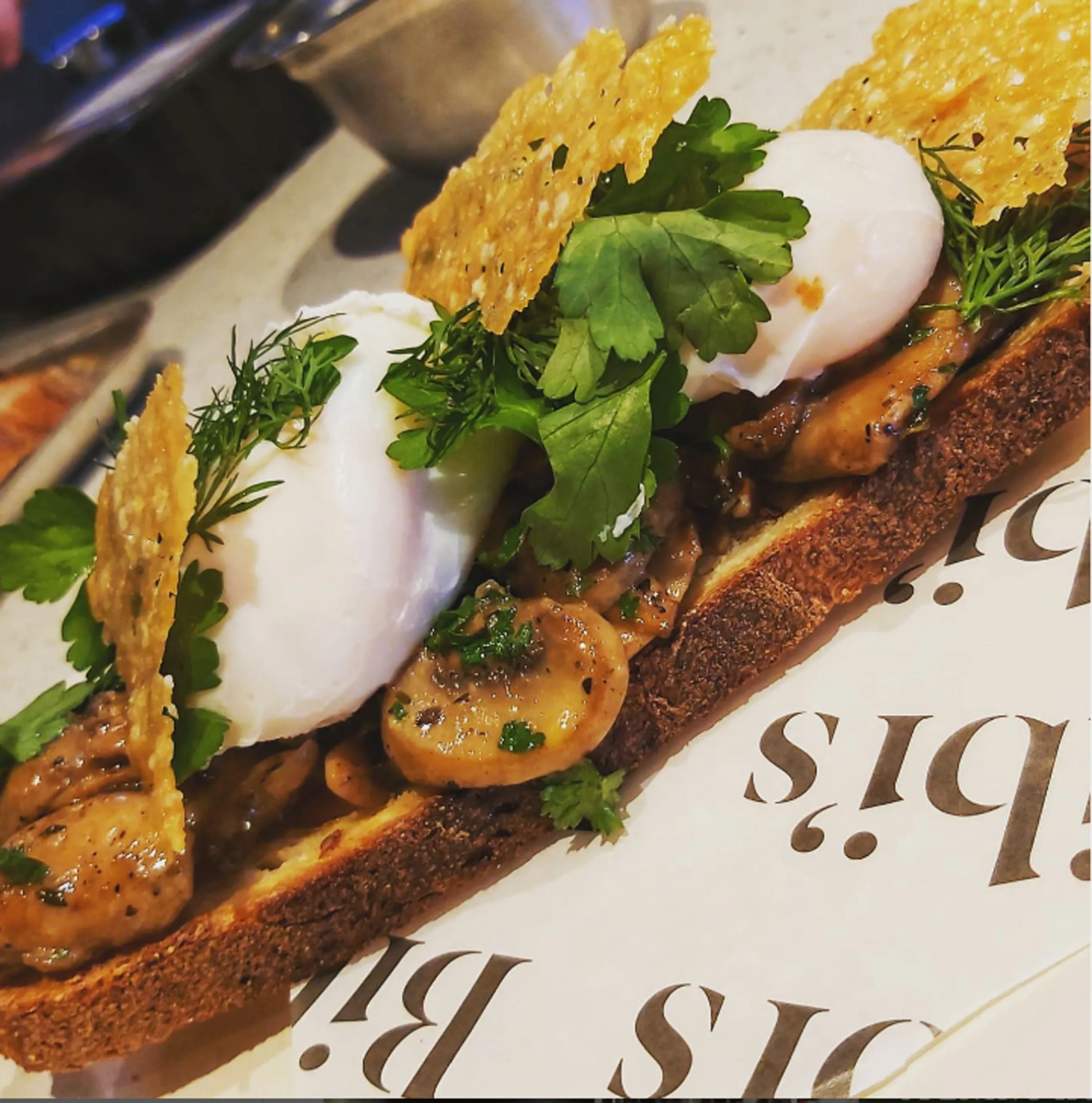 A gourmet toast topped with poached eggs, mushrooms, herbs, and crispy cheese crisps.