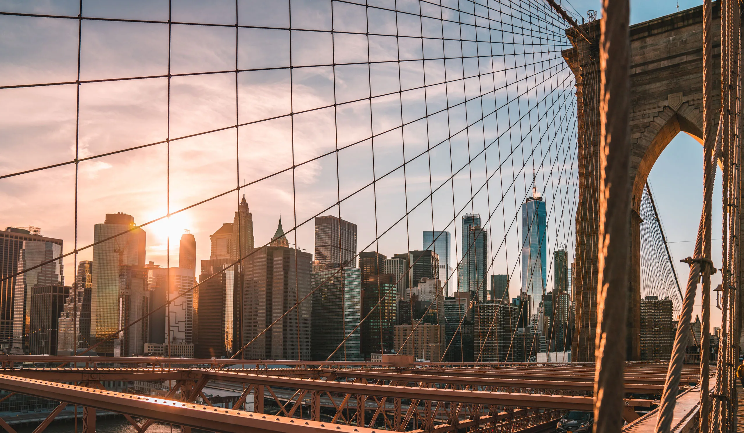 Brooklyn Bridge cables frame Manhattan skyline at sunset, highlighting modern skyscrapers.