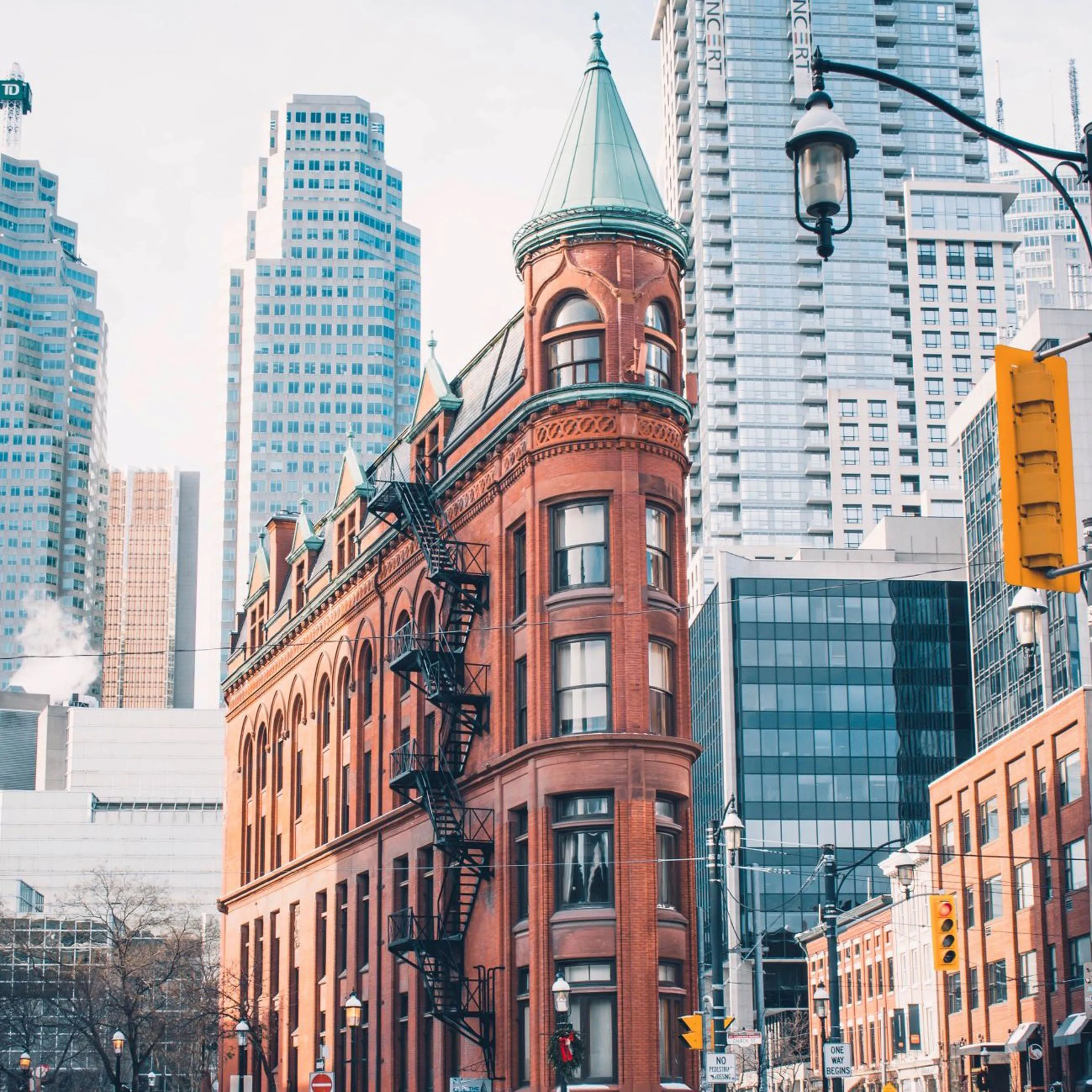Historic red-brick flatiron building contrasts with modern skyscrapers in an urban cityscape.
