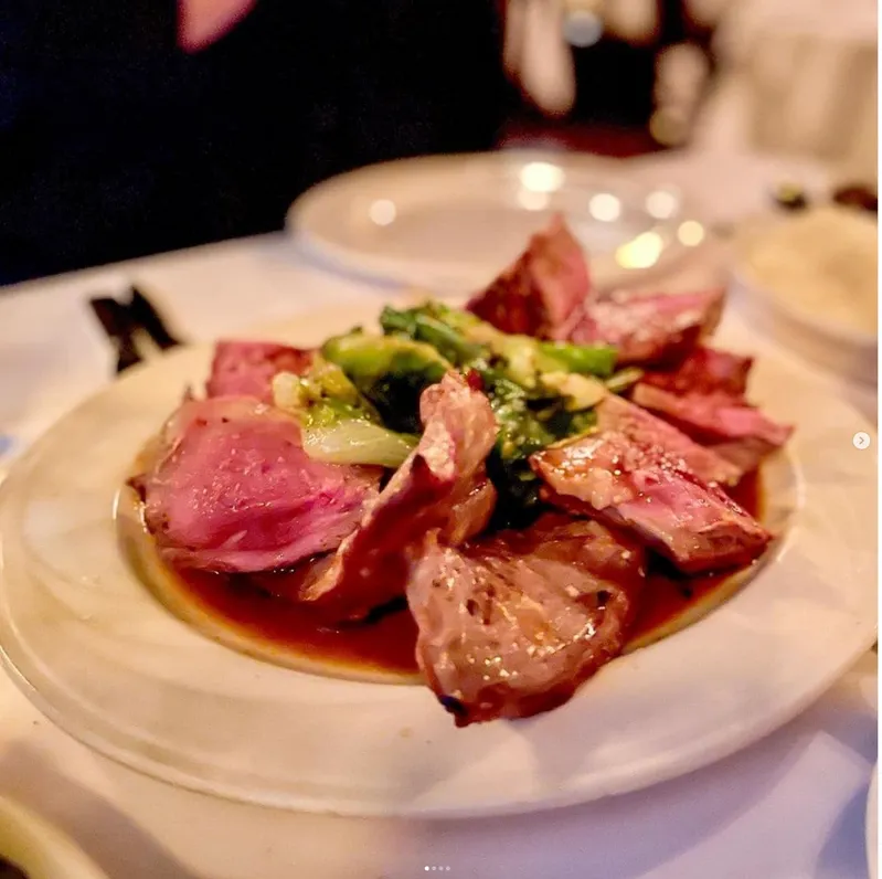 A plated dish featuring sliced medium-rare meat and sautéed greens, served in a rich sauce.