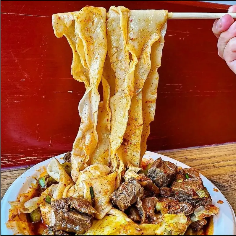 Wide, hand-pulled noodles coated in spicy sauce, served with tender beef chunks and vegetables.