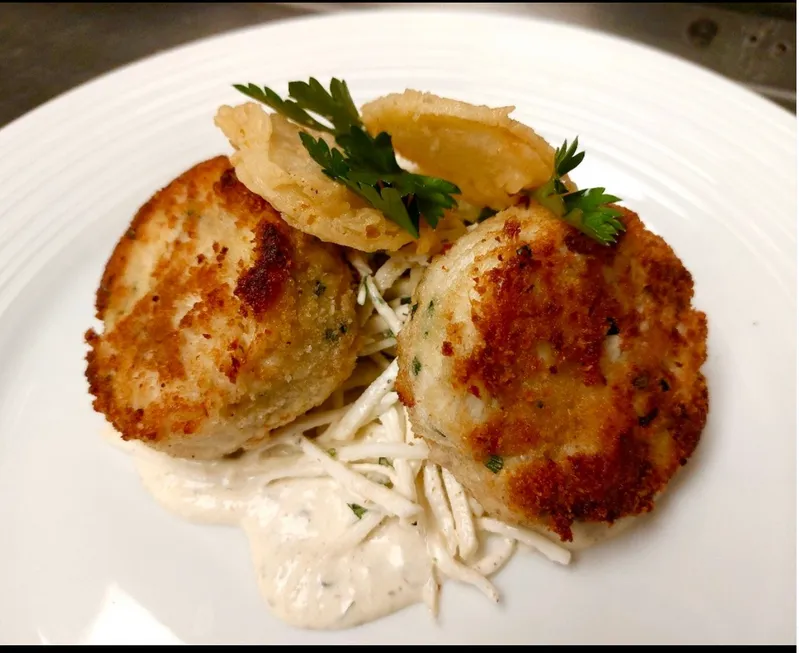 Golden crab cakes on creamy slaw, garnished with parsley and crispy onion rings.