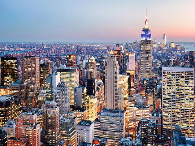 A vibrant cityscape featuring skyscrapers, including the illuminated Empire State Building at dusk.