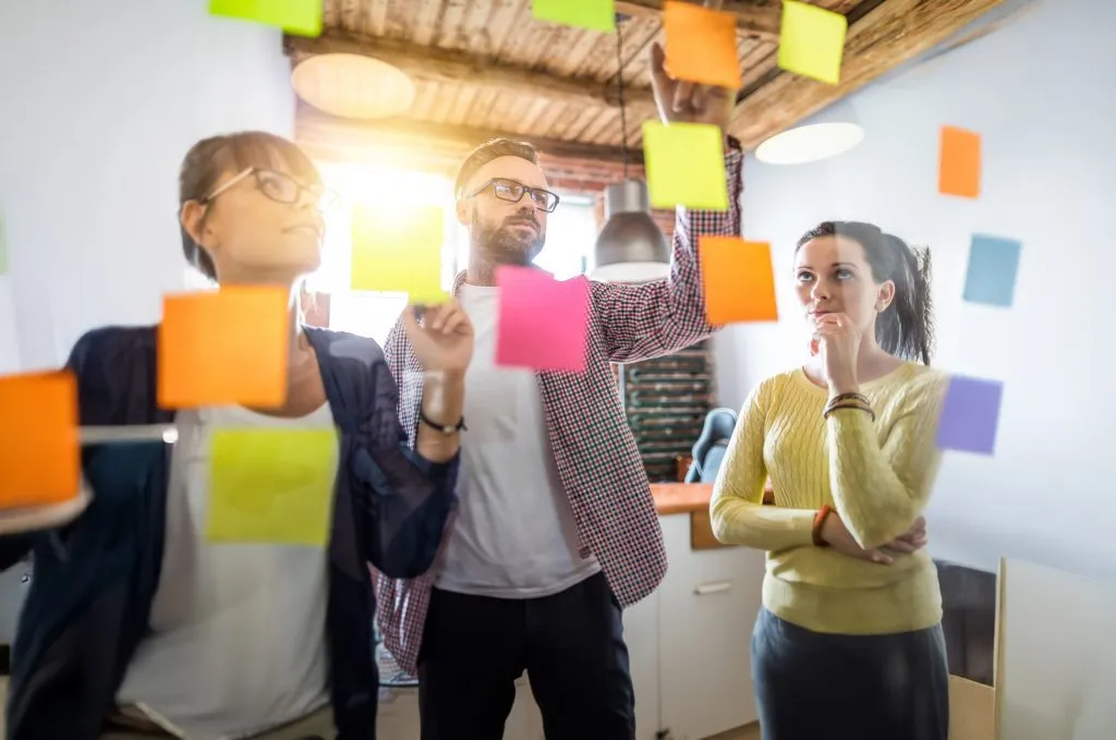 Group of three co workers working together organizing sticky notes.