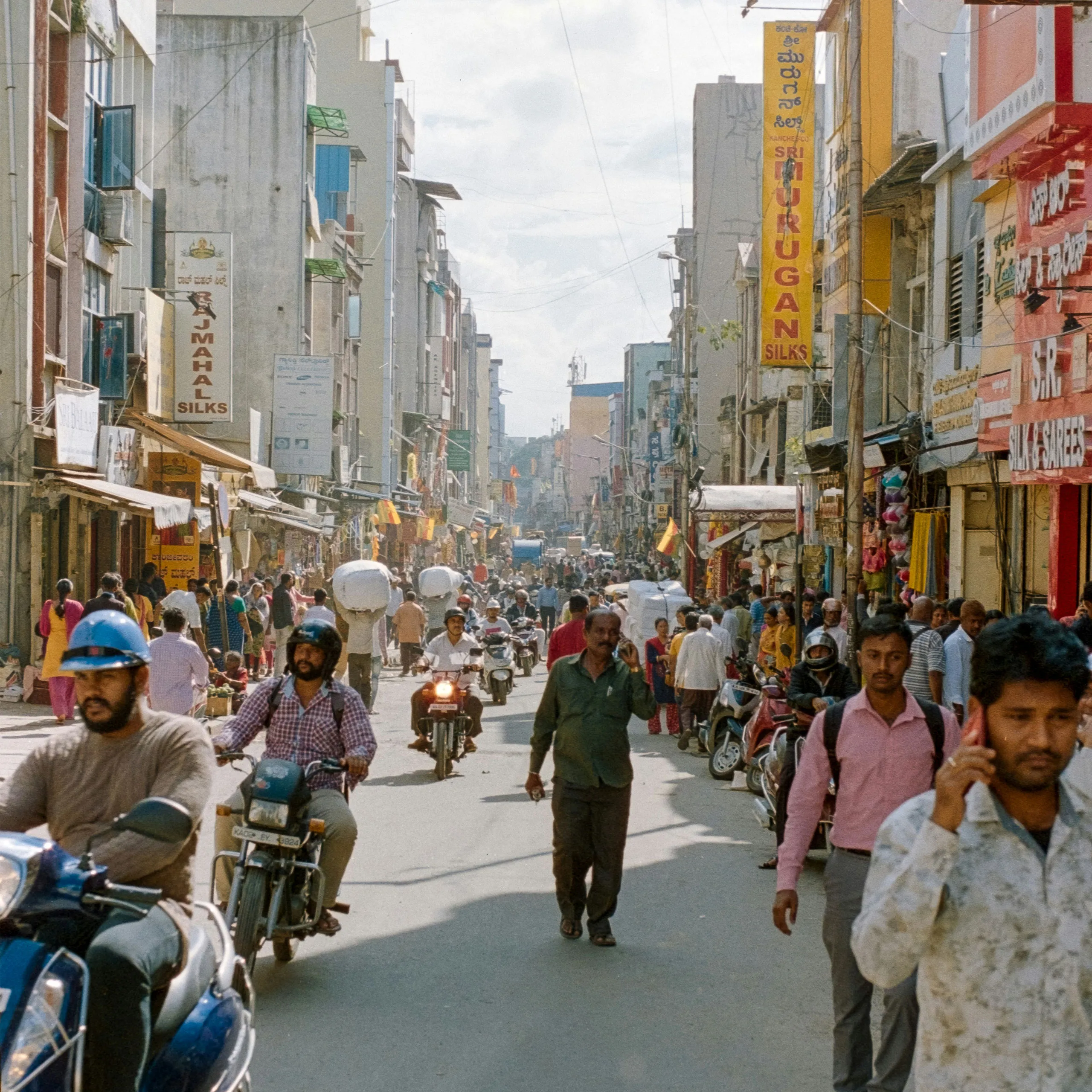 A bustling urban street with shops, pedestrians, motorcycles, and vibrant signage in multiple languages.