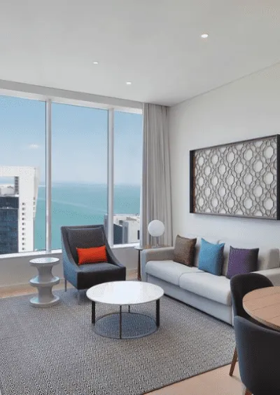 Modern living room with ocean view, neutral tones, sleek furniture, and geometric decor.
