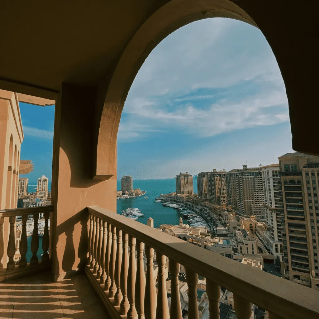 An arched balcony frames a marina view with modern buildings under a clear blue sky.