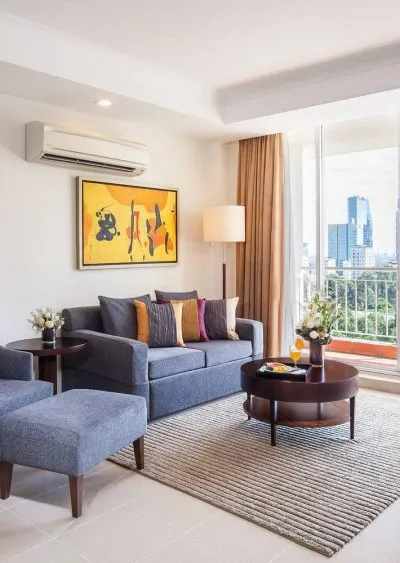 Modern living room with gray furniture, colorful art, and city view through large windows.