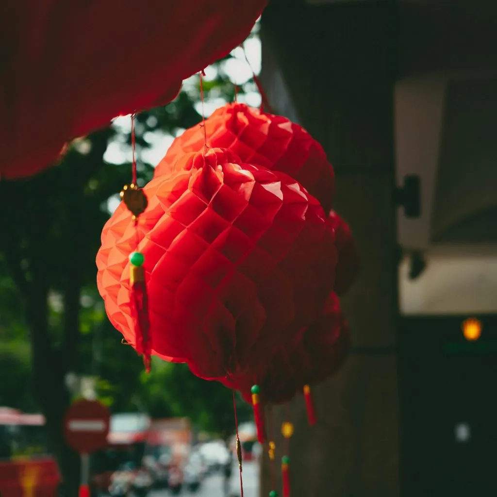 Red paper lanterns hang outdoors, creating a festive atmosphere with blurred greenery in the background.