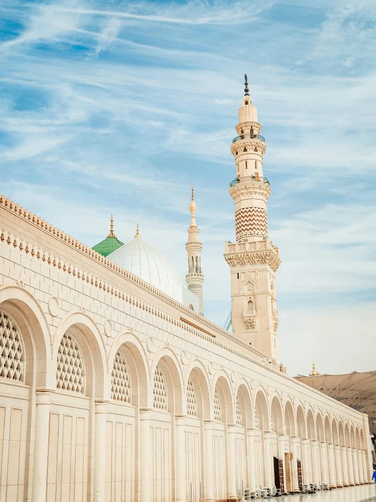 The Prophet's Mosque in Medina features elegant arches, domes, and a towering minaret under a clear sky.