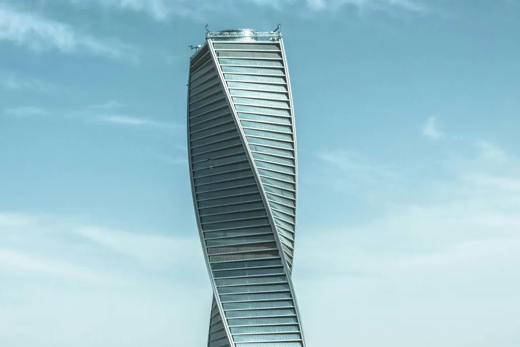 A modern, twisted skyscraper with a sleek glass facade stands against a clear blue sky.