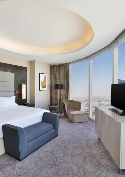 Modern hotel room with curved windows, elegant furnishings, and cityscape views.