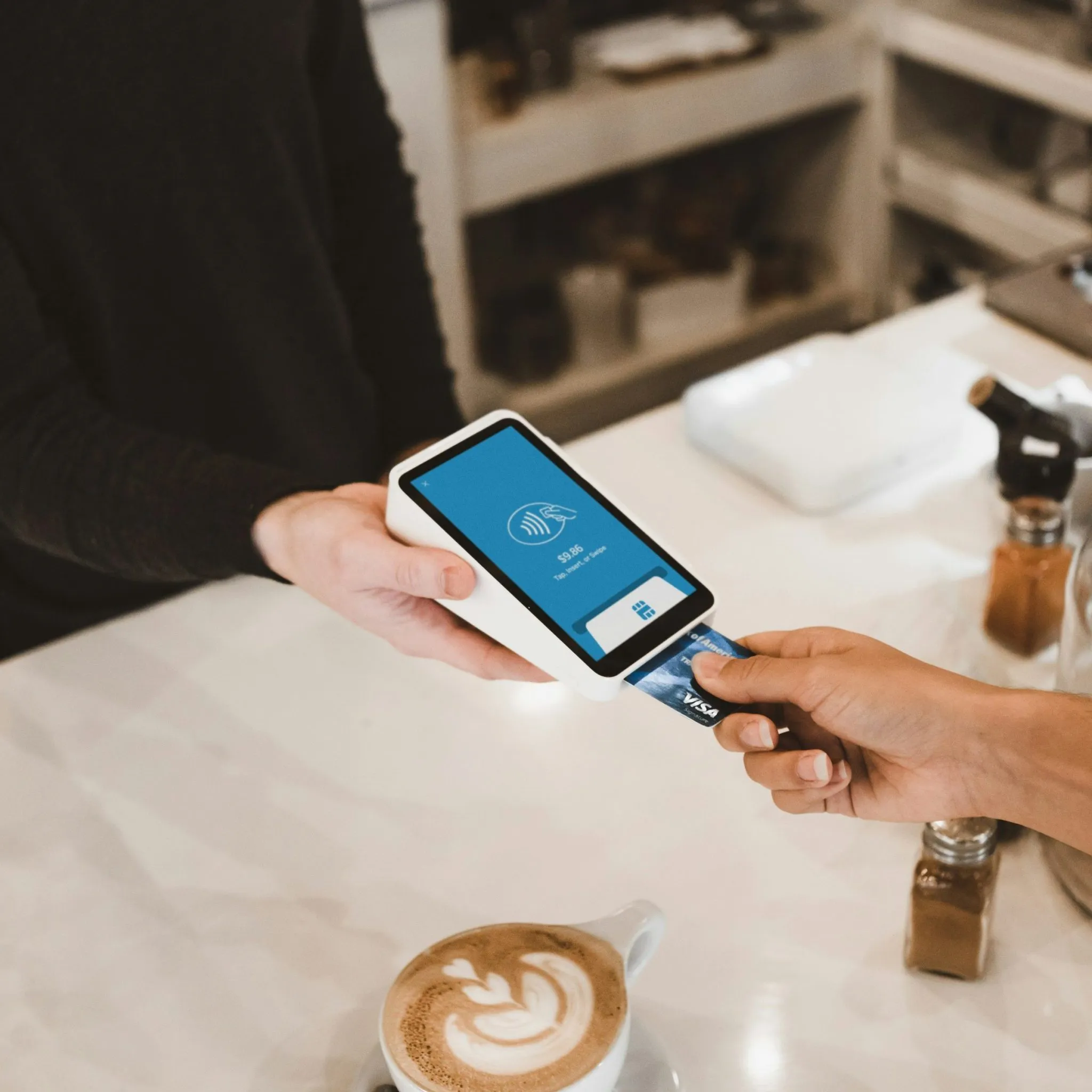 A person makes a payment using a Visa card on a modern point-of-sale terminal at a café.