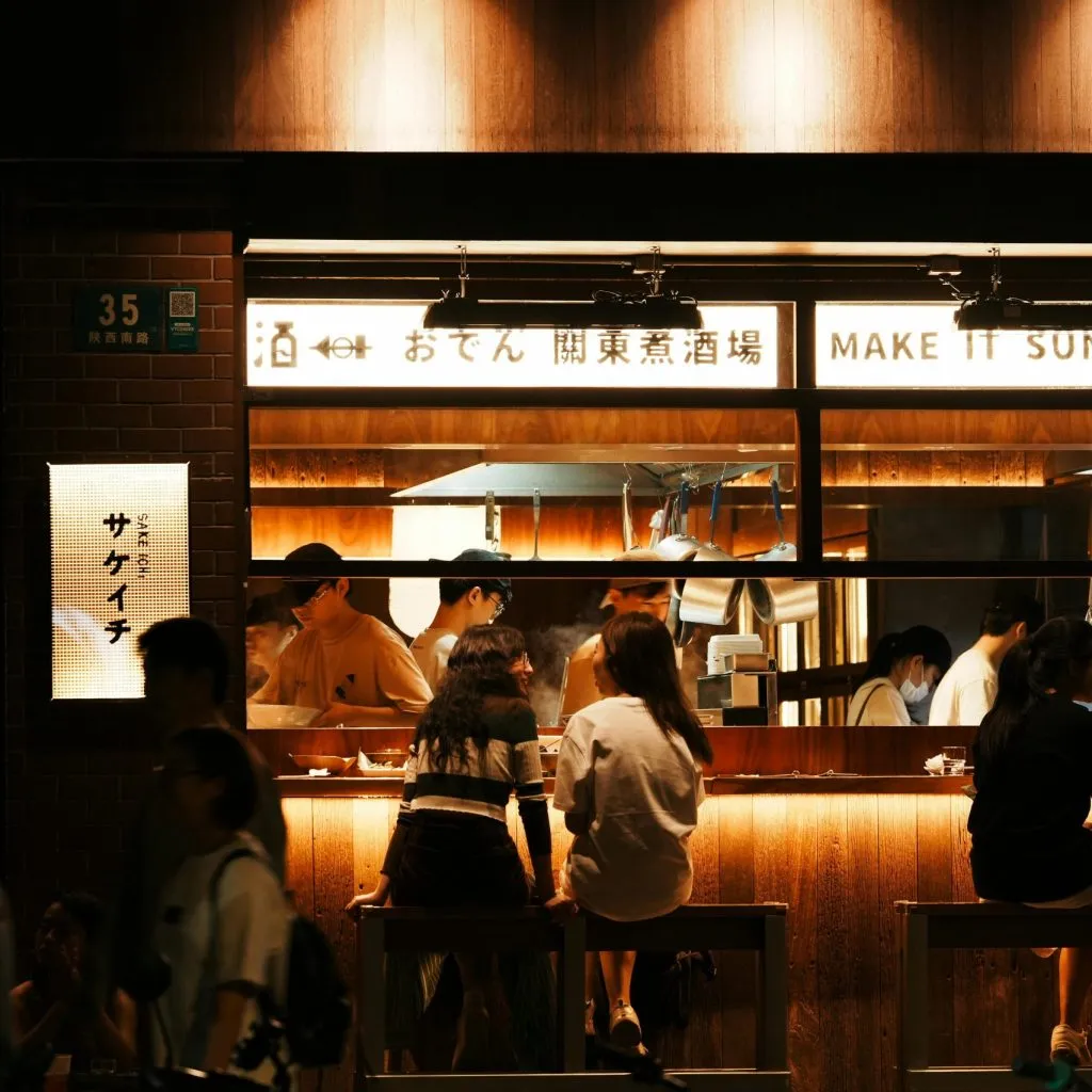 A warmly lit Japanese-style eatery with patrons seated at a wooden counter, enjoying the ambiance.