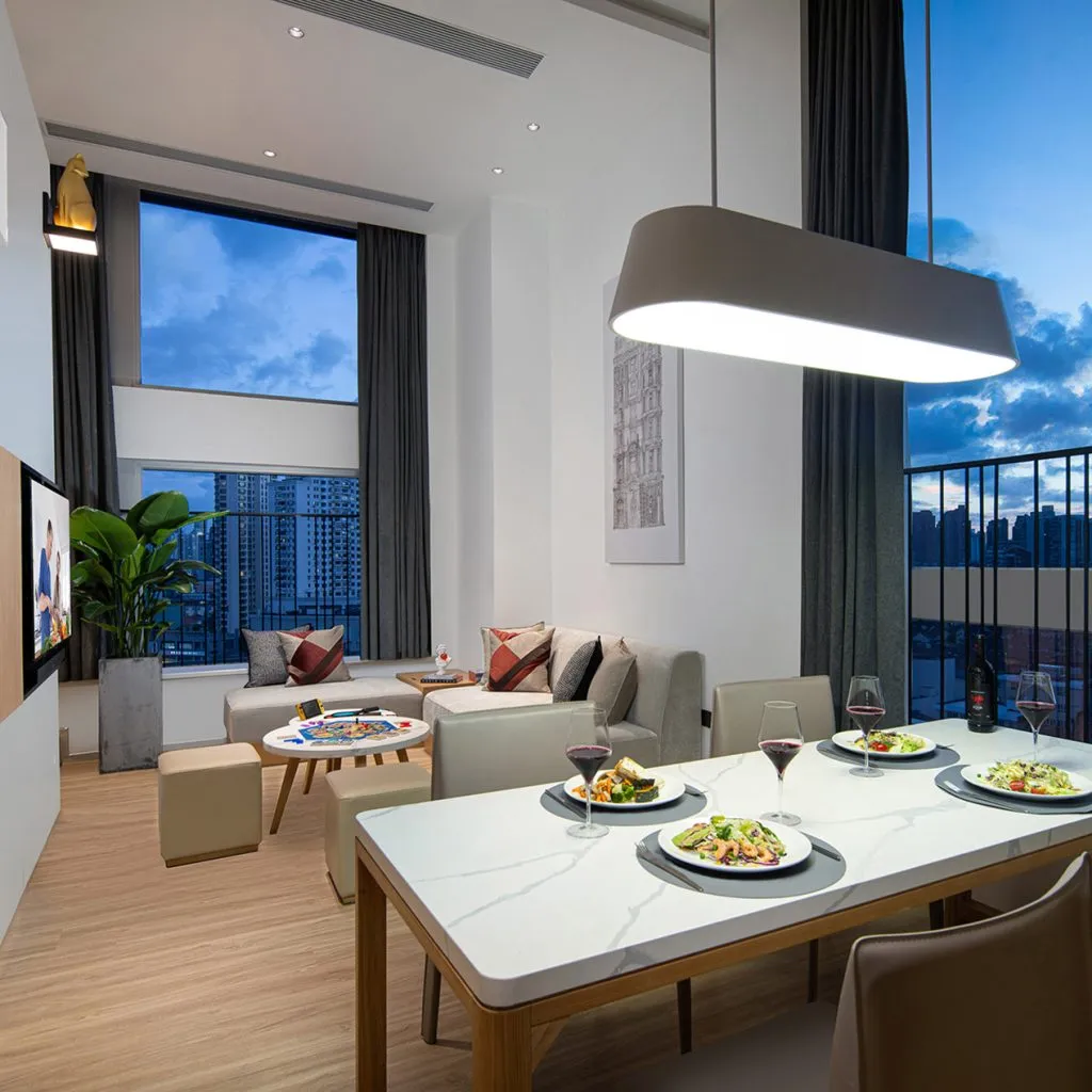 Modern dining and living area with city views, sleek furniture, and warm ambient lighting.