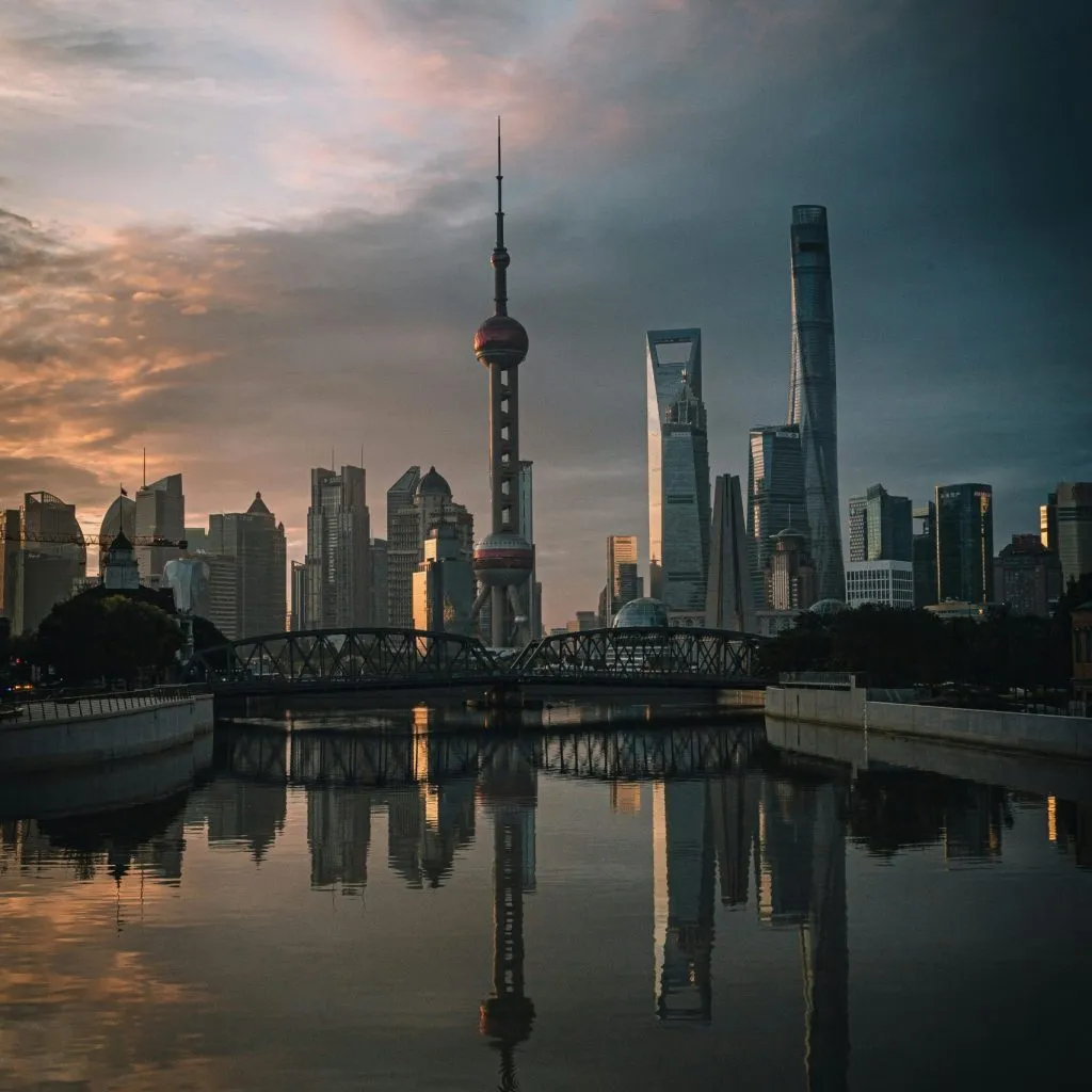 Shanghai skyline at dusk, featuring iconic skyscrapers reflected in a calm river.
