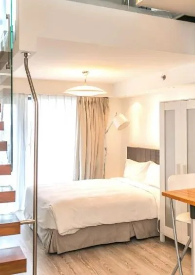 Modern loft-style bedroom with wooden stairs, white furnishings, and natural light.