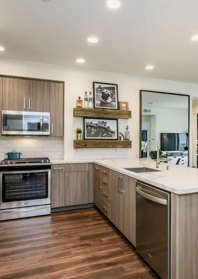 Modern kitchen with wood cabinets, white countertops, open shelving, and stainless steel appliances.