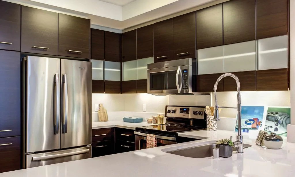 Modern kitchen with dark cabinets, stainless steel appliances, and a sleek white countertop.