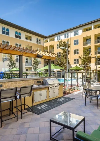 Modern apartment courtyard with BBQ grill, seating, pool, and landscaped surroundings.