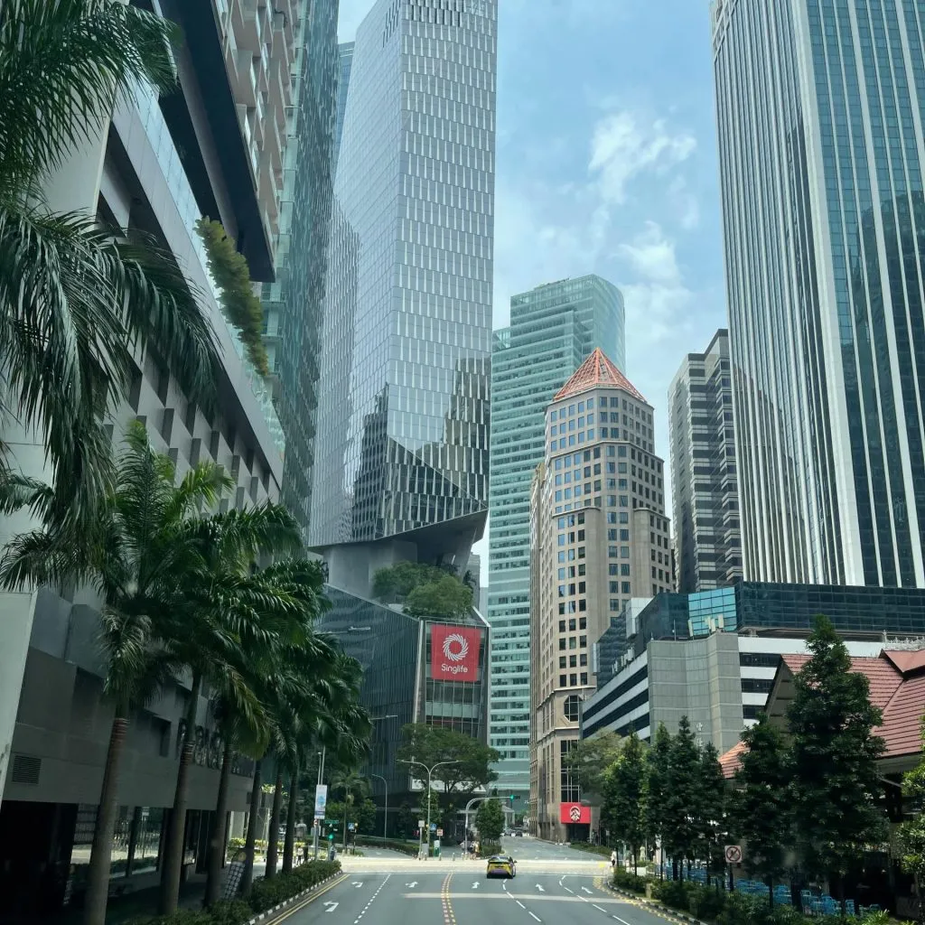 Modern skyscrapers and lush greenery line a quiet urban street under a clear blue sky.