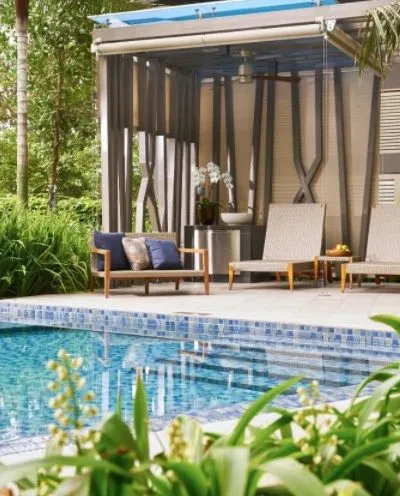 A serene poolside setting with lounge chairs, lush greenery, and a modern cabana in the background.